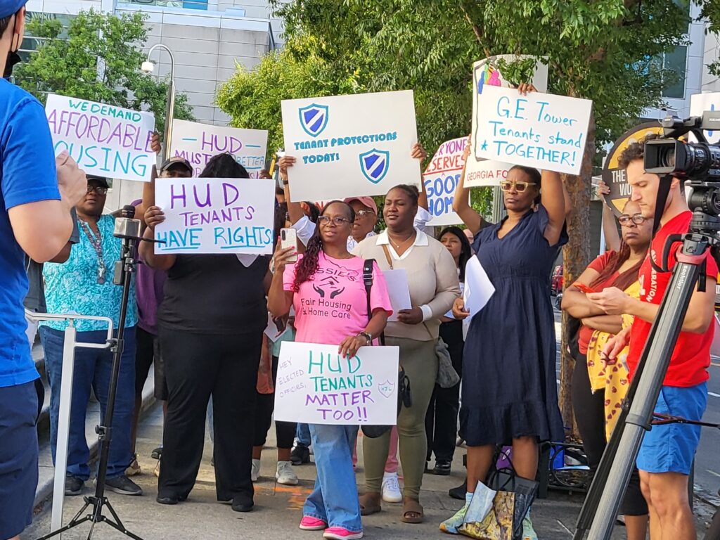 Photo of Diana Brown holding and other protestors holding signs at a rally in front of HUD offices. 