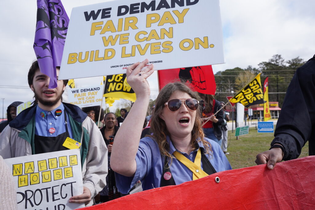 A picture of a waffle House worker holding a sign that reads " We demand fair pay we can build lives on."